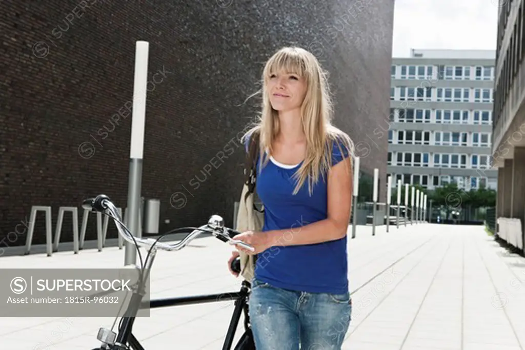 Germany, Cologne, Young woman with bicycle, smiling
