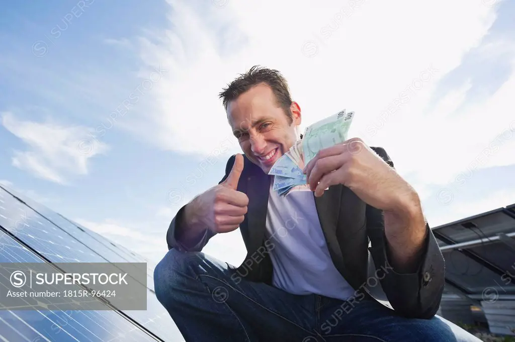 Germany, Munich, Man with euro notes in solar plant, smiling, portrait