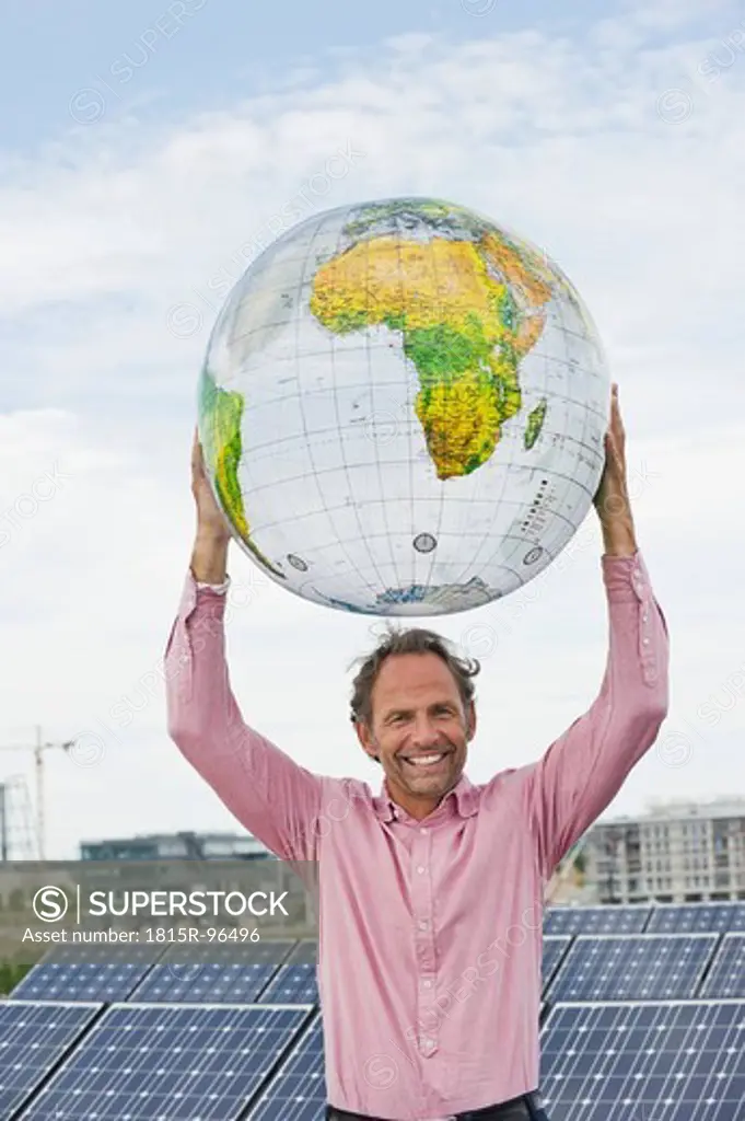 Germany, Munich, Mature man holding globe in solar plant, smiling, portrait