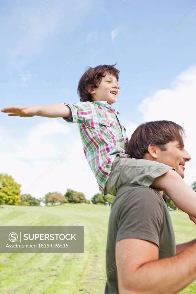 Germany, Bavaria, Father carrying son on shoulder in park, smiling