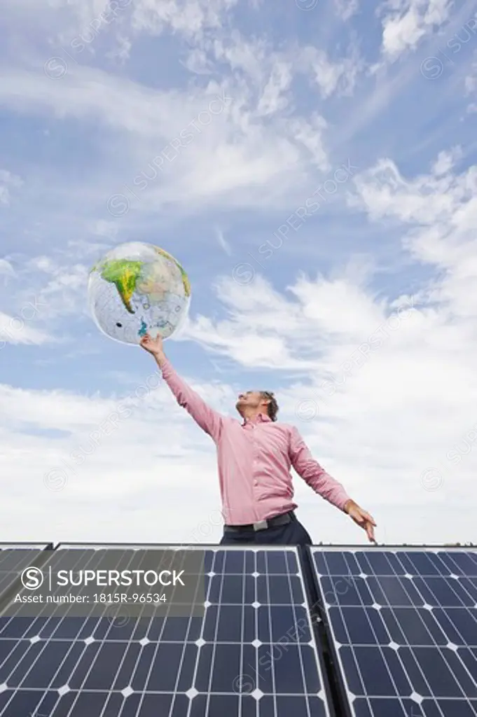 Germany, Munich, Mature man balancing globe on finger in solar plant