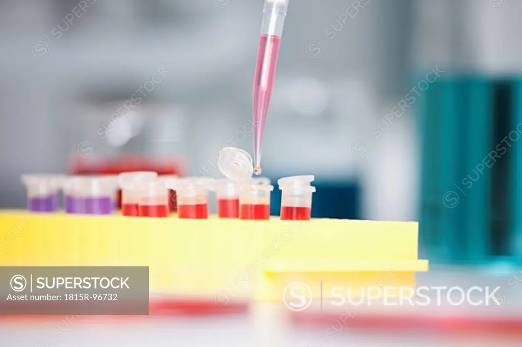 Germany, Bavaria, Munich, Pipette pouring liquid into test tubes for medical research