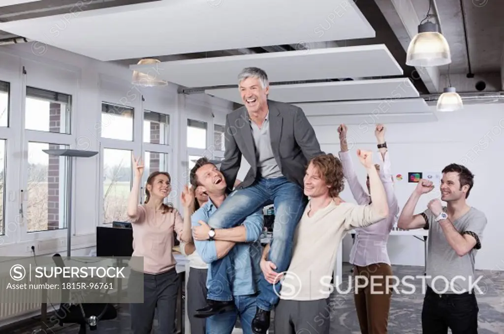 Germany, Bavaria, Munich, Colleagues carrying mature man on shoulder, smiling