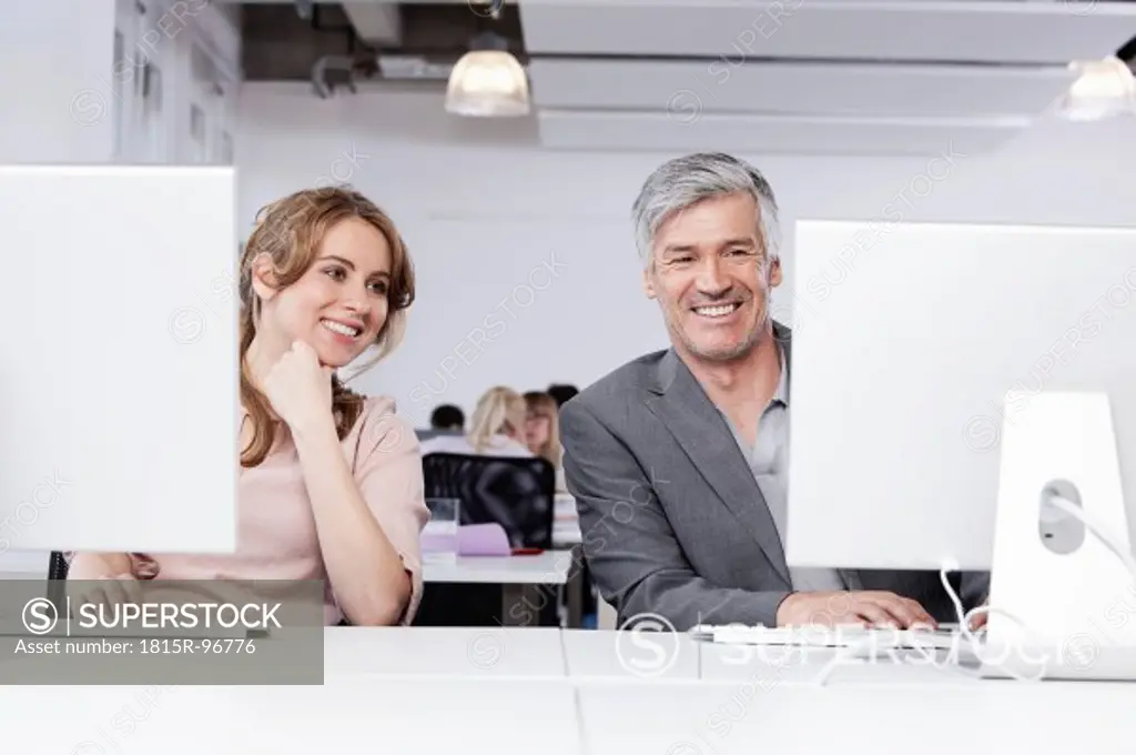 Germany, Bavaria, Munich, Man and woman using computer in office, smiling