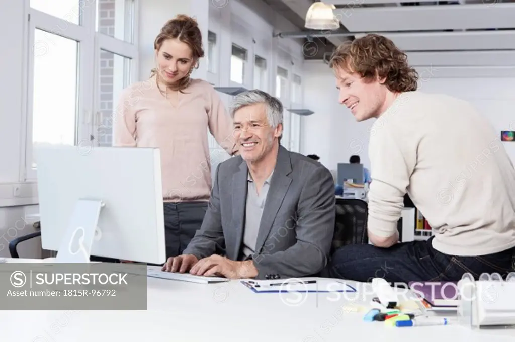 Germany, Bavaria, Munich, Men and woman using computer in office, smiling