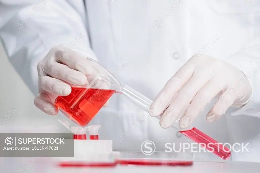 Germany, Bavaria, Munich, Scientist pouring red liquid in test tube for medical research in laboratory