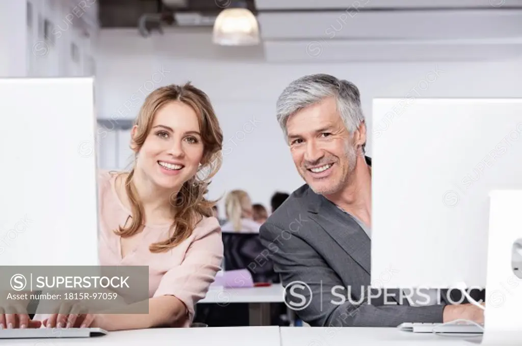 Germany, Bavaria, Munich, Man and woman using computer in office, smiling, portrait