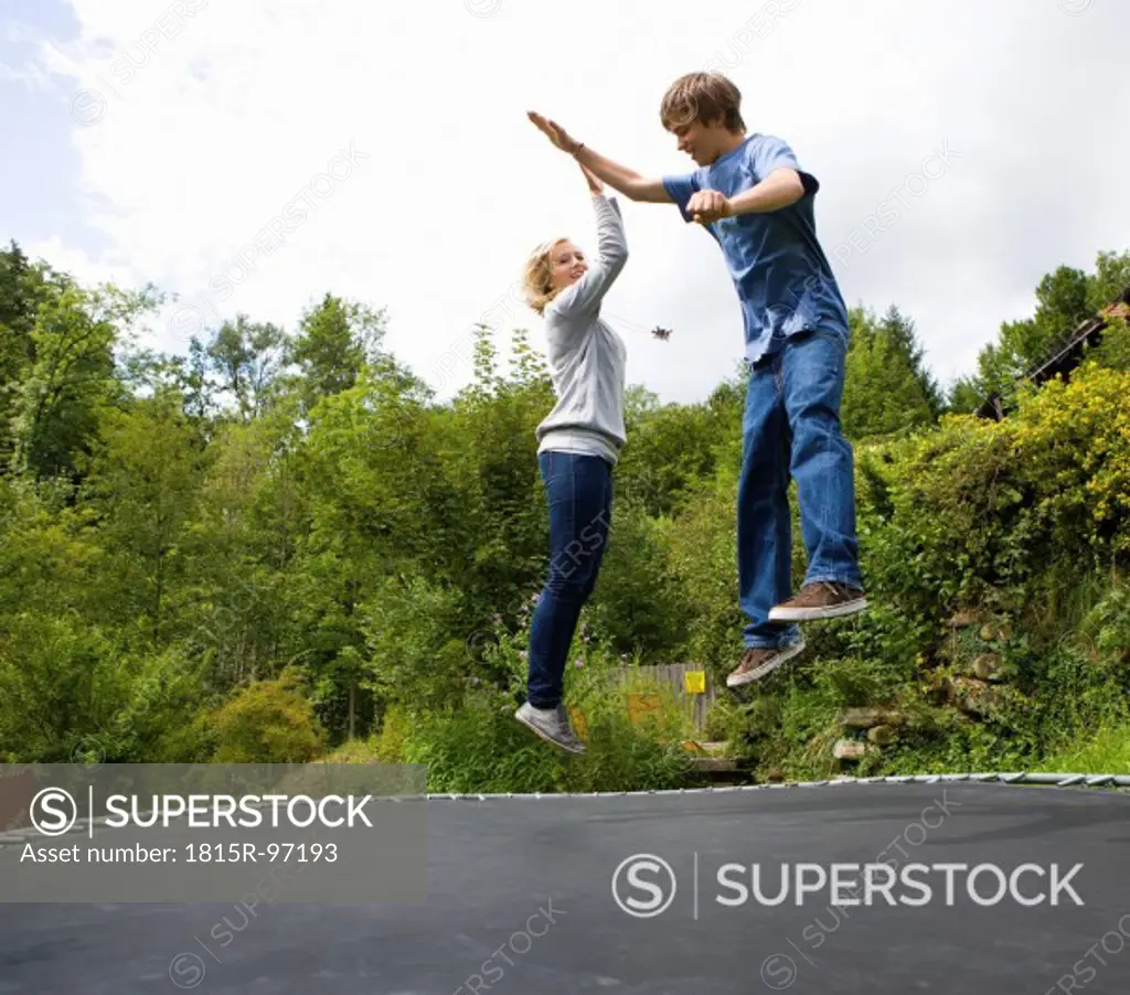 Austria, Young man and woman jumping on trampoline