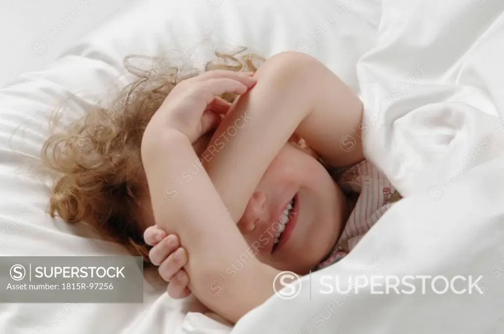 Girl lying on bed and covering her eyes, smiling