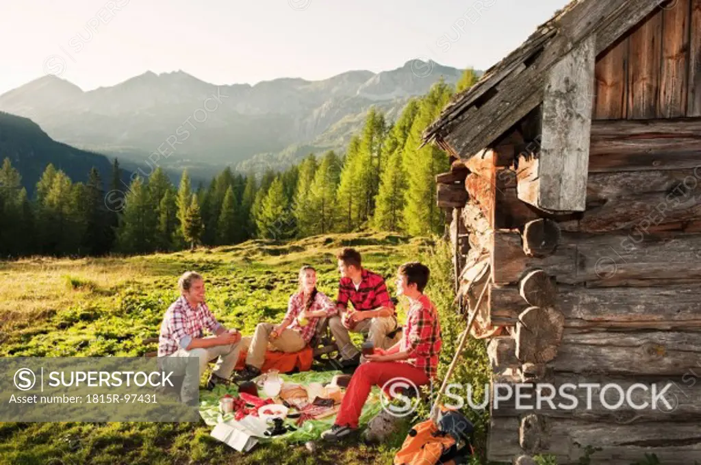 Austria, Salzburg County, Men and women having picnic near alpine hut at sunset