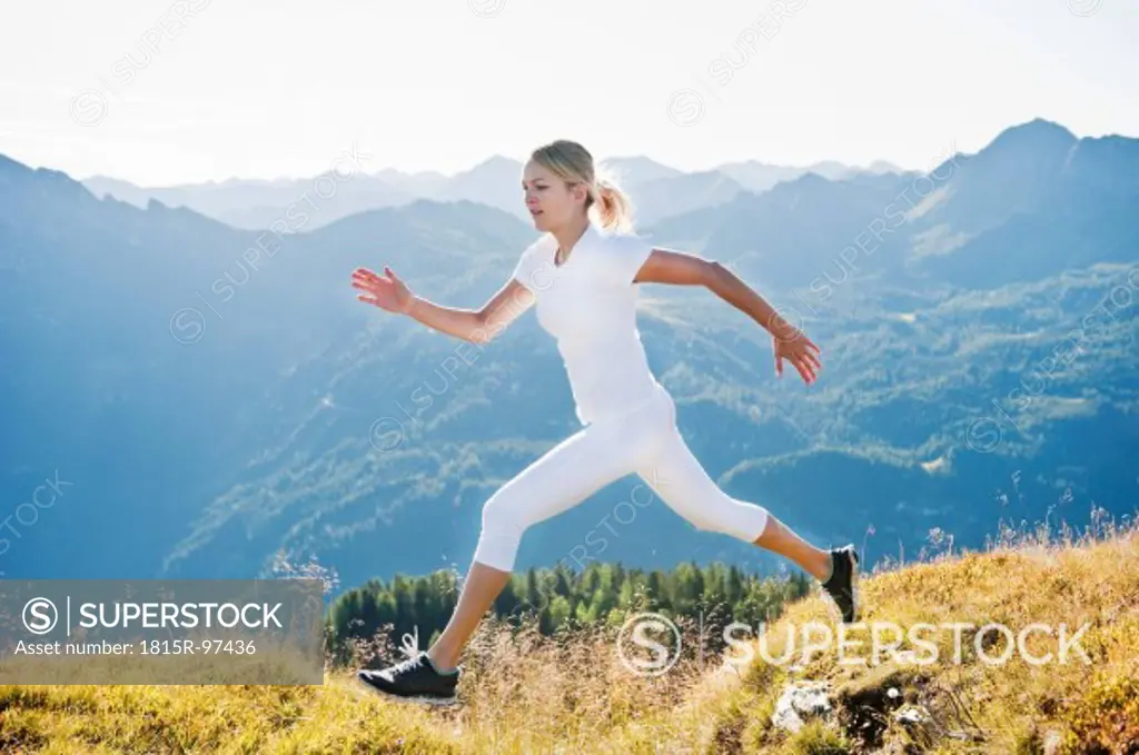 Austria, Salzburg County, Young woman running and jumping in alpine meadow
