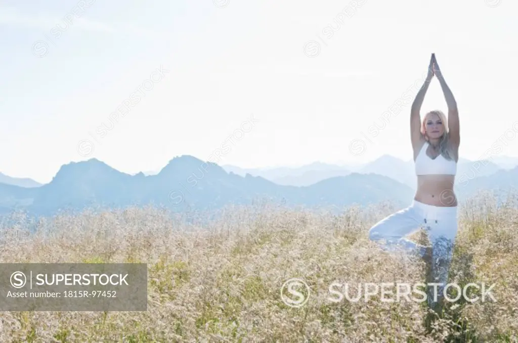 Austria, Salzburg County, Young woman standing in alpine meadow and doing meditation