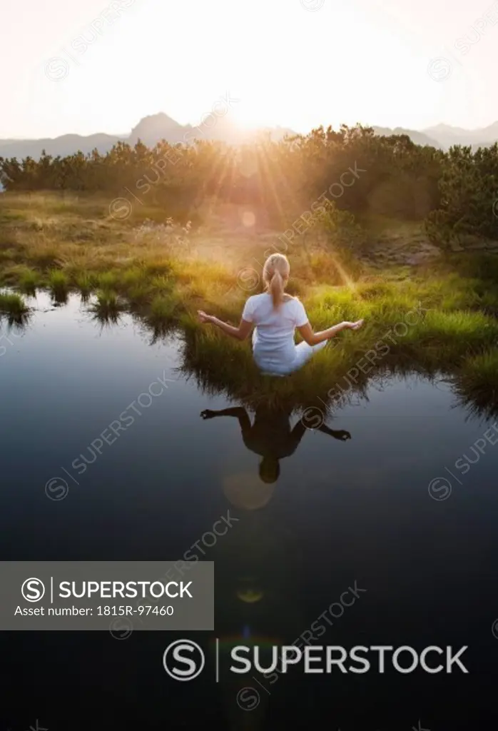 Austria, Salzburg County, Young woman sitting near mountain lake and doing meditation