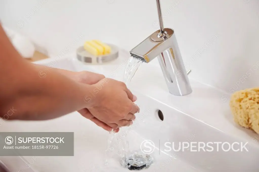 Germany, Bavaria, Young woman washing hands in bathroom sink