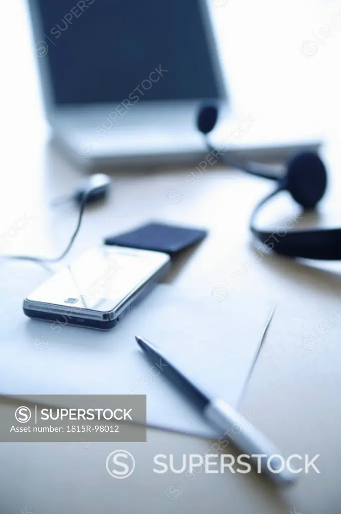Cell phone, head set, pen and laptop on office table, close up