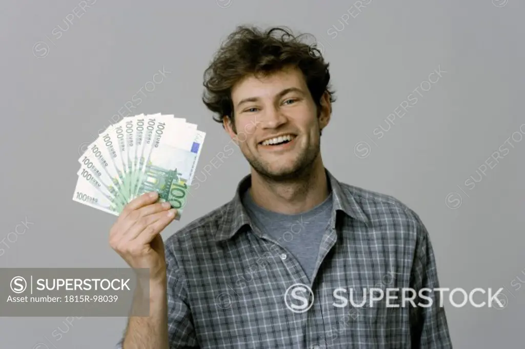 Young man holding 100 Euro bills against grey background