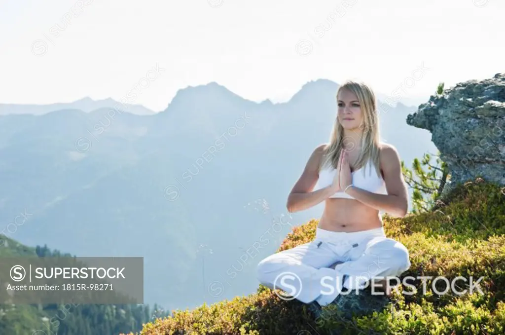 Austria, Salzburg County, Young woman sitting on rock and doing meditation