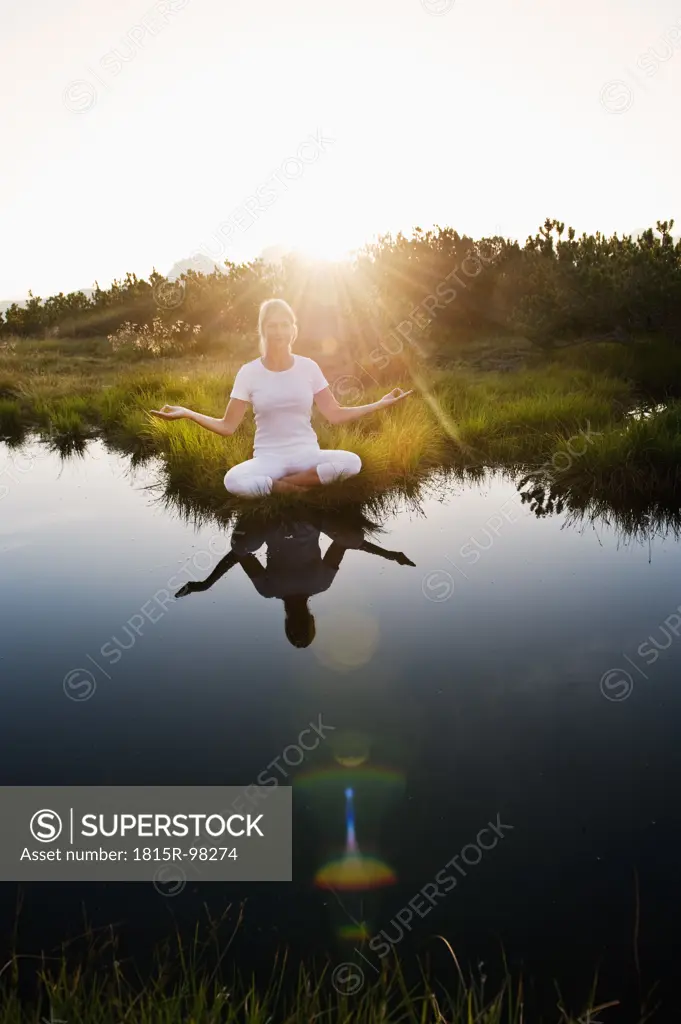 Austria, Salzburg County, Young woman sitting near mountain lake and doing meditation