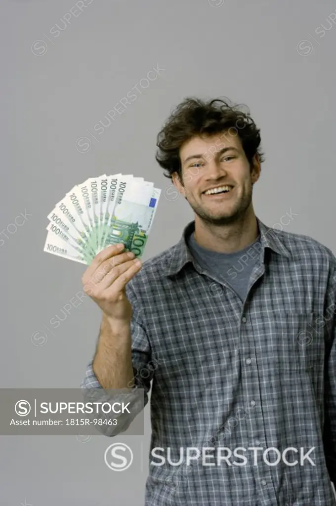 Young man holding 100 Euro bills against grey background