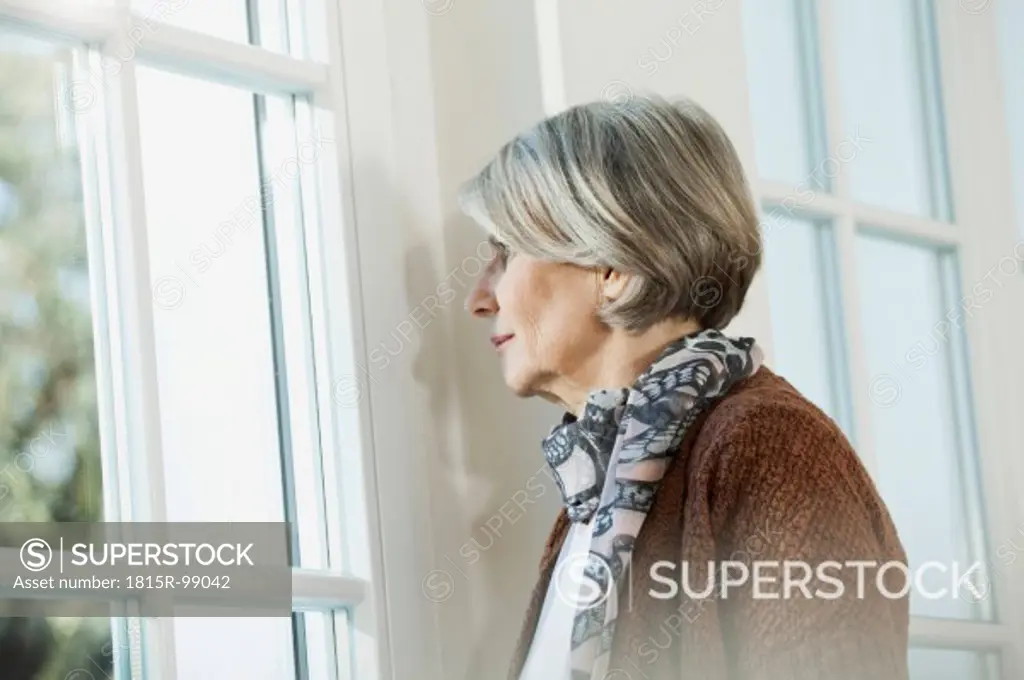 Germany, Berlin, Senior woman looking through window