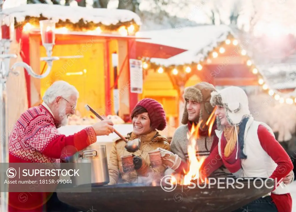 Austria, Salzburg, Senior man serving drink to young people at christmas market, smiling