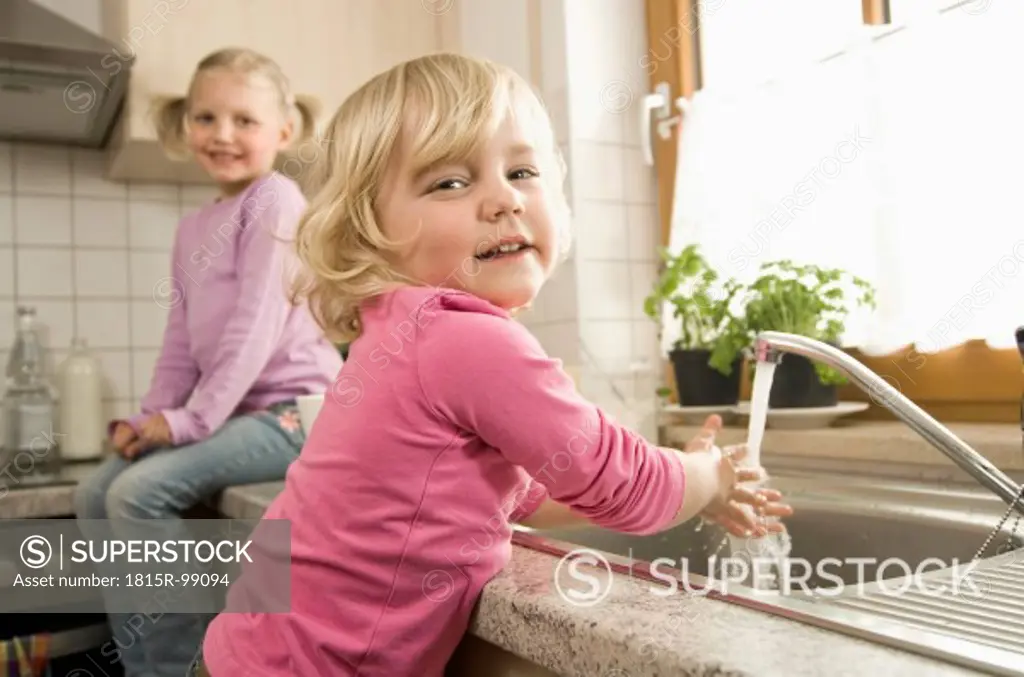 Girl washing hands, sister sitting in background