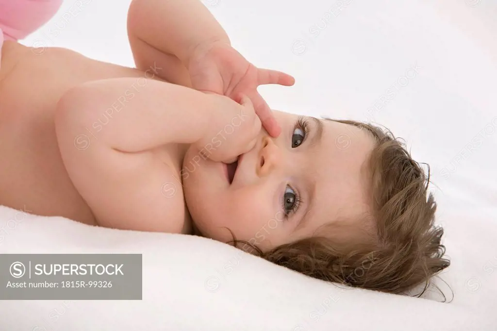 Baby girl lying on back with finger in mouth, smiling