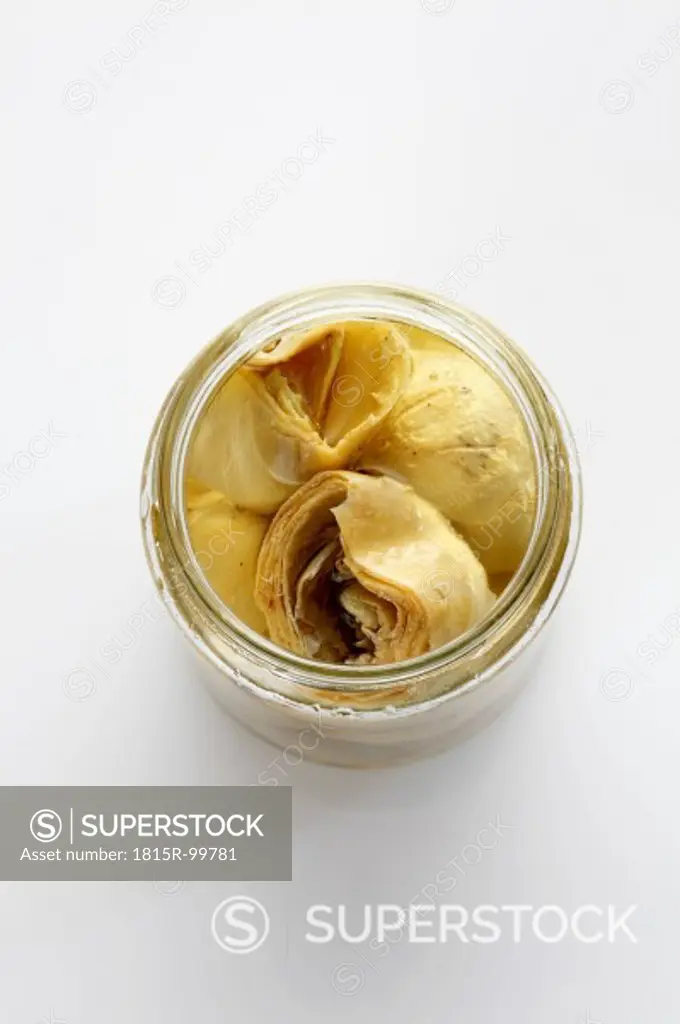 Preserved artischoke hearts with olive oil in glass jar on white background
