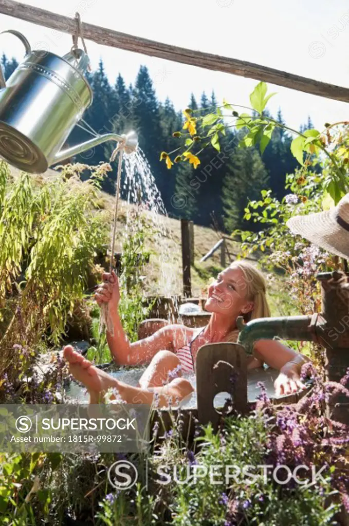 Austria, Salzburg, Flachau, Young woman taking bath with watering can in tun