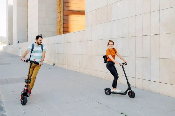 Couple riding electric scooters on pavement