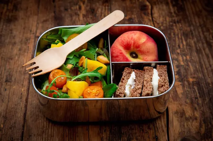 Close-up of healthy salad with sandwiches and fruit in lunch box on table