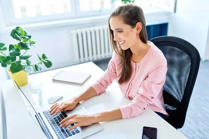 Smiling young woman working on laptop in home office