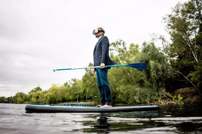 Businessman wearing VR glasses on SUP board on a lake