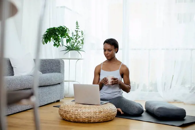 Woman sitting on gym mat at home using laptop