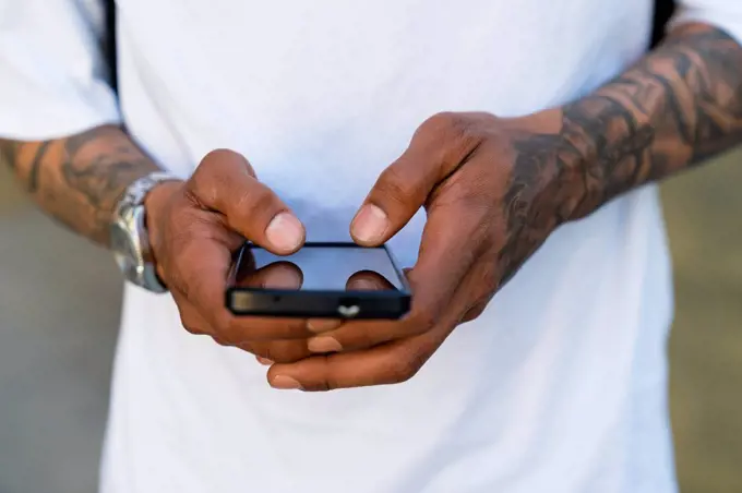 Hands of tattooed man using smartphone, close-up