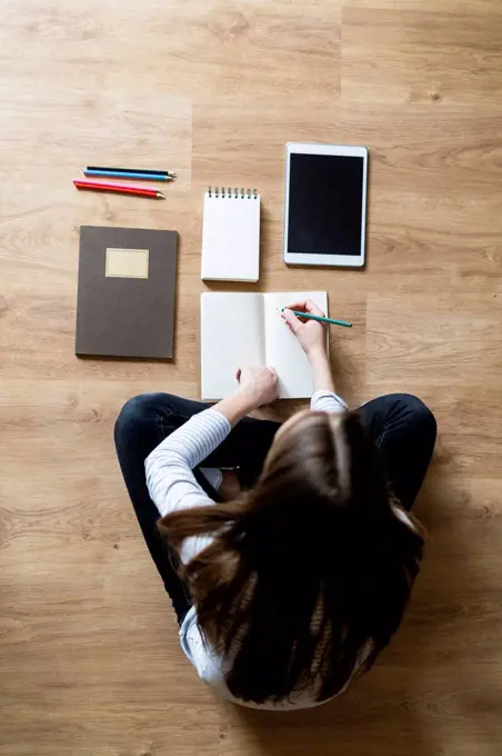 Top view of young woman sitting on the floor at home taking notes
