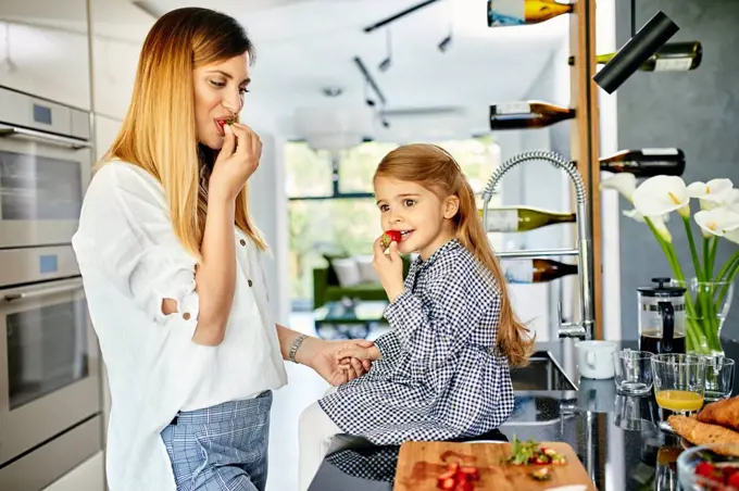 Mother and daughter eating strawberries in modern kitchen