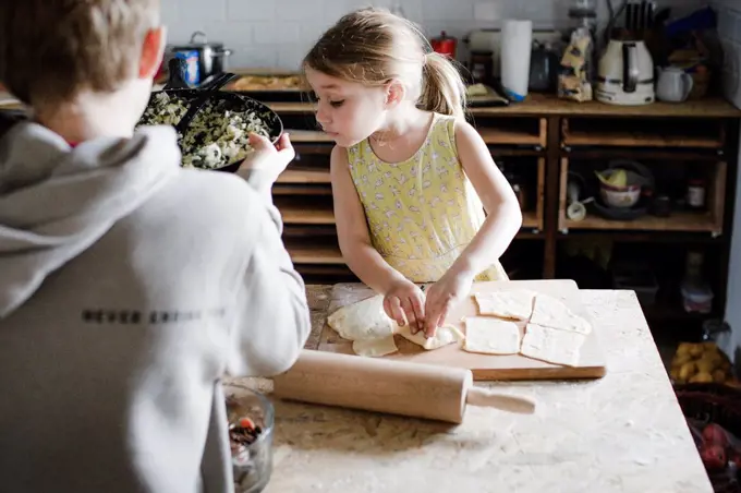 Little girl and her older brother preparing stuffed pastry in the kitchen