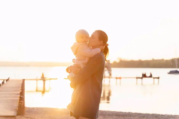 Germany, Bavaria, Herrsching, mother carrying daughter at the lakeshore at sunset