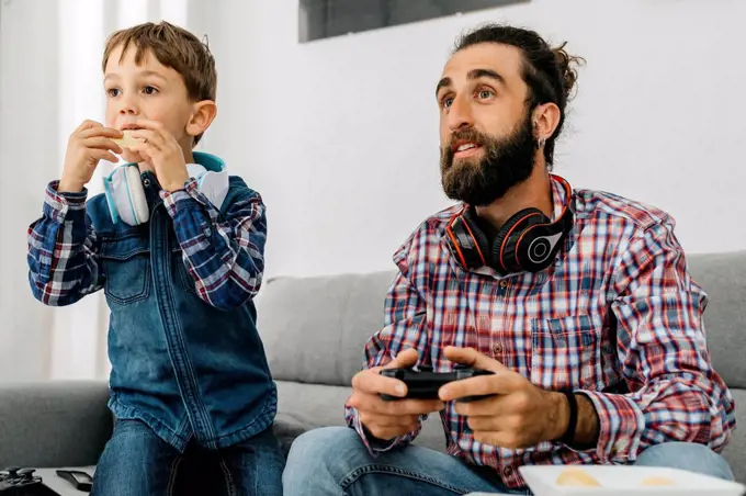 Portrait of father and son on the couch playing computer game