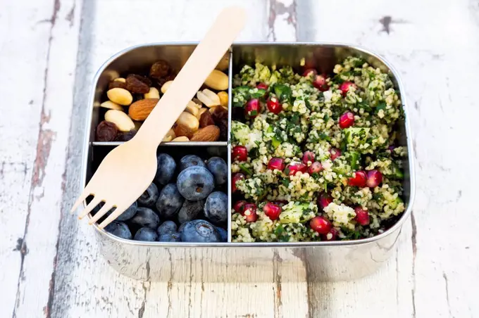 Lunchbox with bulgur herbs salad with pomegranate seeds, taboule, blueberries and trail mIx