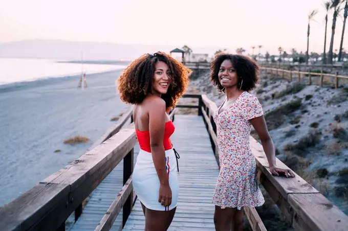 Young smiling women walking together near to the beach, turning around and looking at camera in the evening