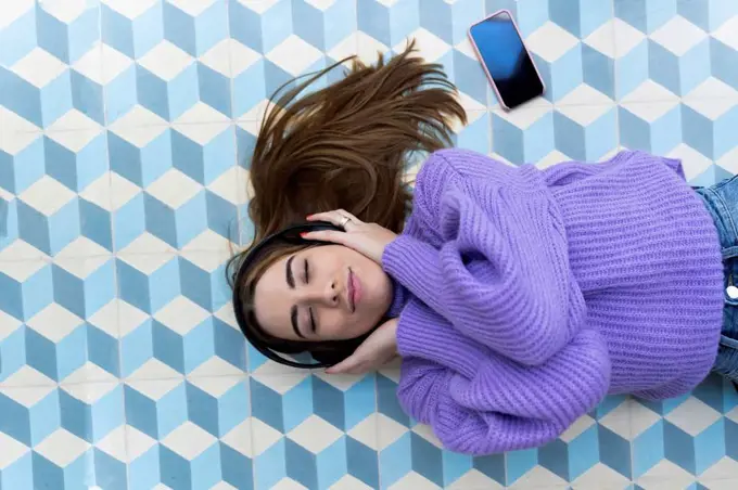 Portrait of young woman with eyes closed lying on the floor listening music with headphones