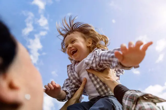 Mother lifting up happy toddler son outdoors