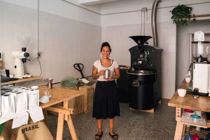 Portrait of smiling woman in a coffee roastery holding coffee pot