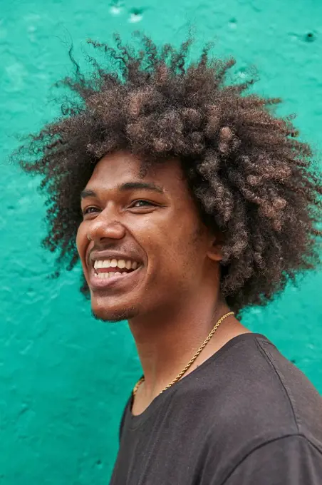 Portrait of laughing young man with afro against green wall