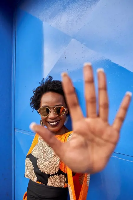 Portrait of smiling woman raising her hand in front of blue background