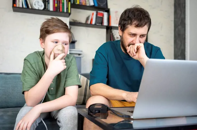 Portrait of father and son sitting together on the couch using laptop