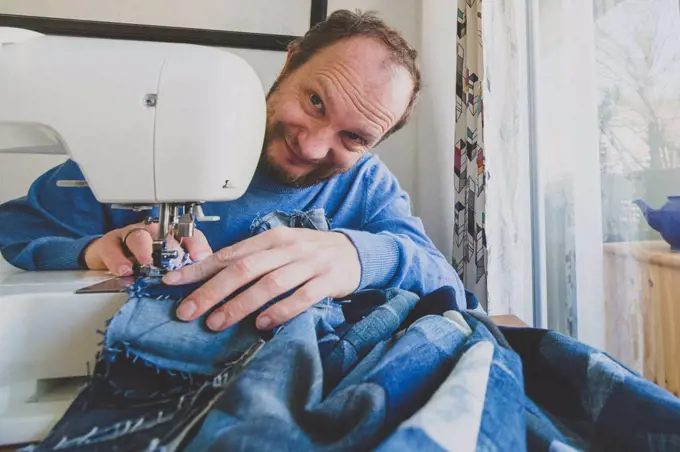 Portrait of smiling man sewing denim quilt at home