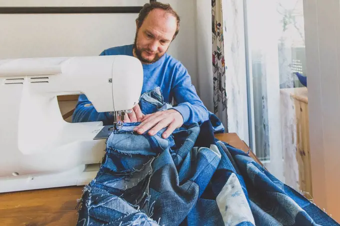 Mature man sewing denim quilt at home